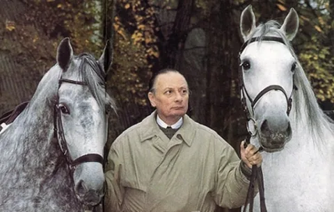 Egon von Neindorff standing between two grey horses, holding their reins